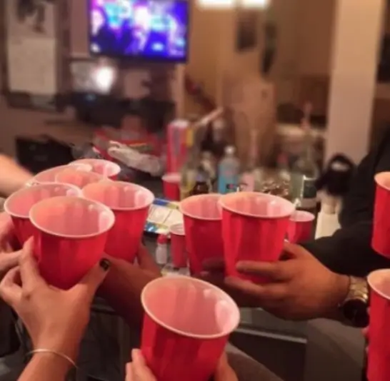 People making a toast in a party with alocohol in red cups.